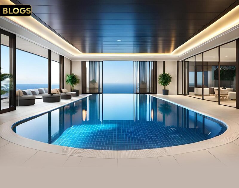 MGI Paradise: Your Premier Living Experience. The image shows a luxurious indoor swimming pool area with a modern design. The pool has a curved shape with a blue-tiled bottom, surrounded by a sleek, white-tiled floor. Large floor-to-ceiling windows offer a stunning view of the ocean, allowing natural light to flood the space. Comfortable seating areas with plush cushions and potted plants add to the serene and elegant ambiance. The ceiling features recessed lighting, enhancing the sophisticated atmosphere of the room.